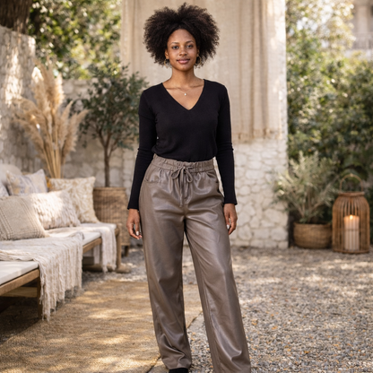 Pantalon large femme en imitation cuir brillant noir, porté sur mannequin avec un top noir, taille élastiquée, coupe fluide, dans un décor extérieur bohème chic et naturel.
